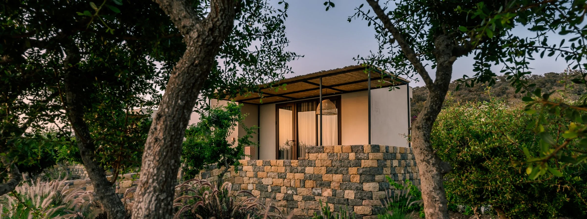 Bungalow Amanblu au crépuscule, entouré d'arganiers et de murs en pierre sèche, Taghazout