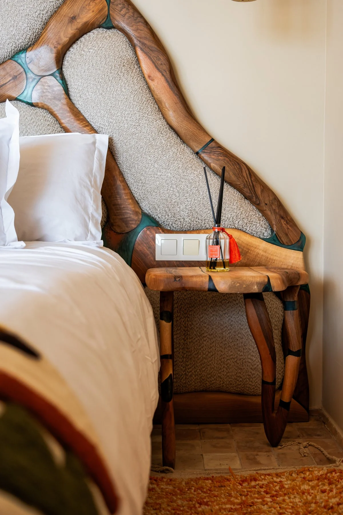 Détail d'un bungalow Amanblu : tête de lit en noyer sculpté incrusté de résine et table de chevet en bois brut