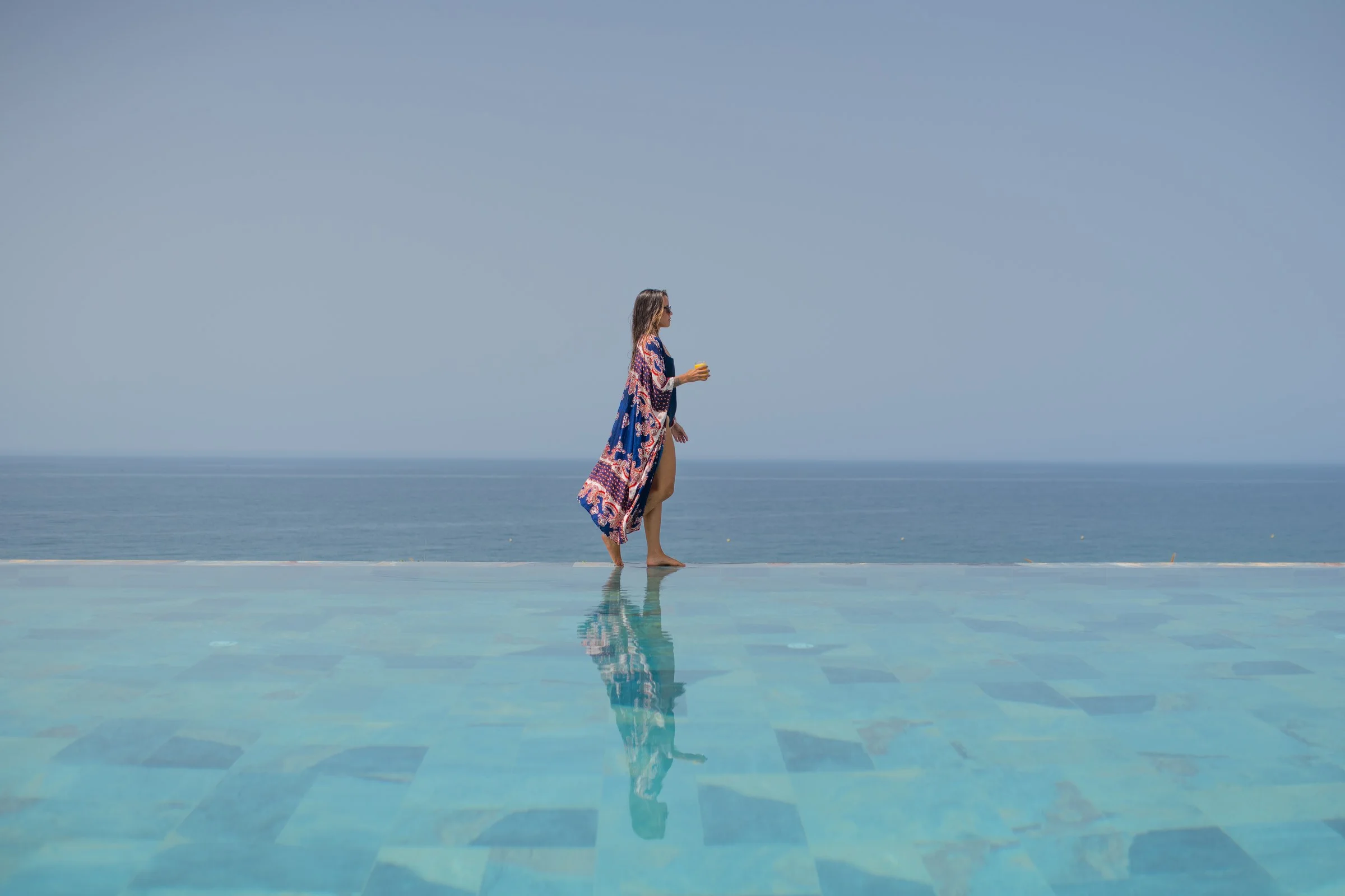 Une voyageuse en kaftan au bord de la piscine à débordement d'Amanblu, l'Atlantique en fond